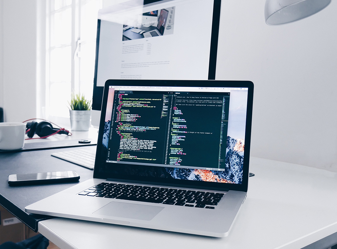 Macbook på ett skrivbord med kod på skärmen.