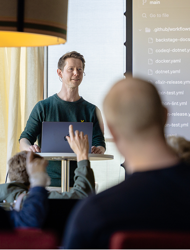 Speaker presenting in front of an audience with code on a large screen.