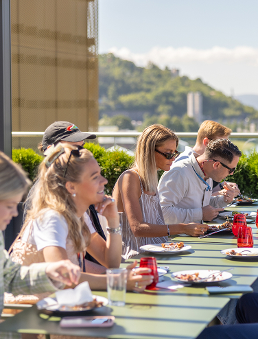 Group of people enjoying a meal together outdoors at a long table on a sunny day.